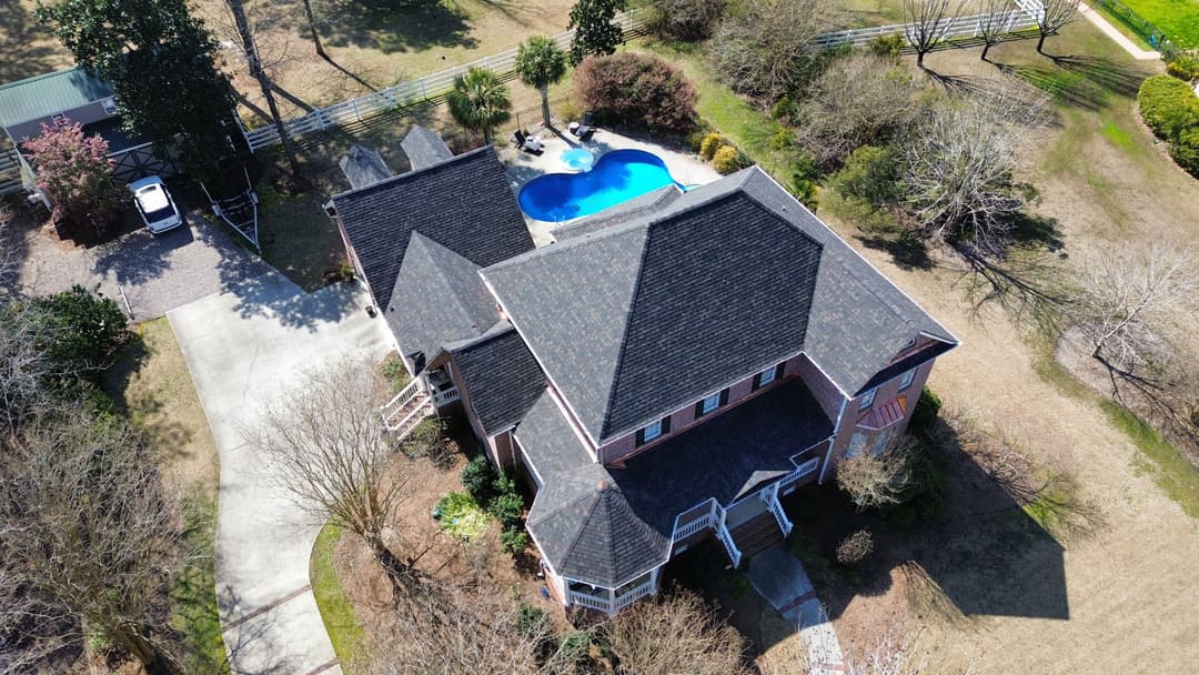 Aerial view of a spacious house with a pool, surrounded by trees and a driveway.