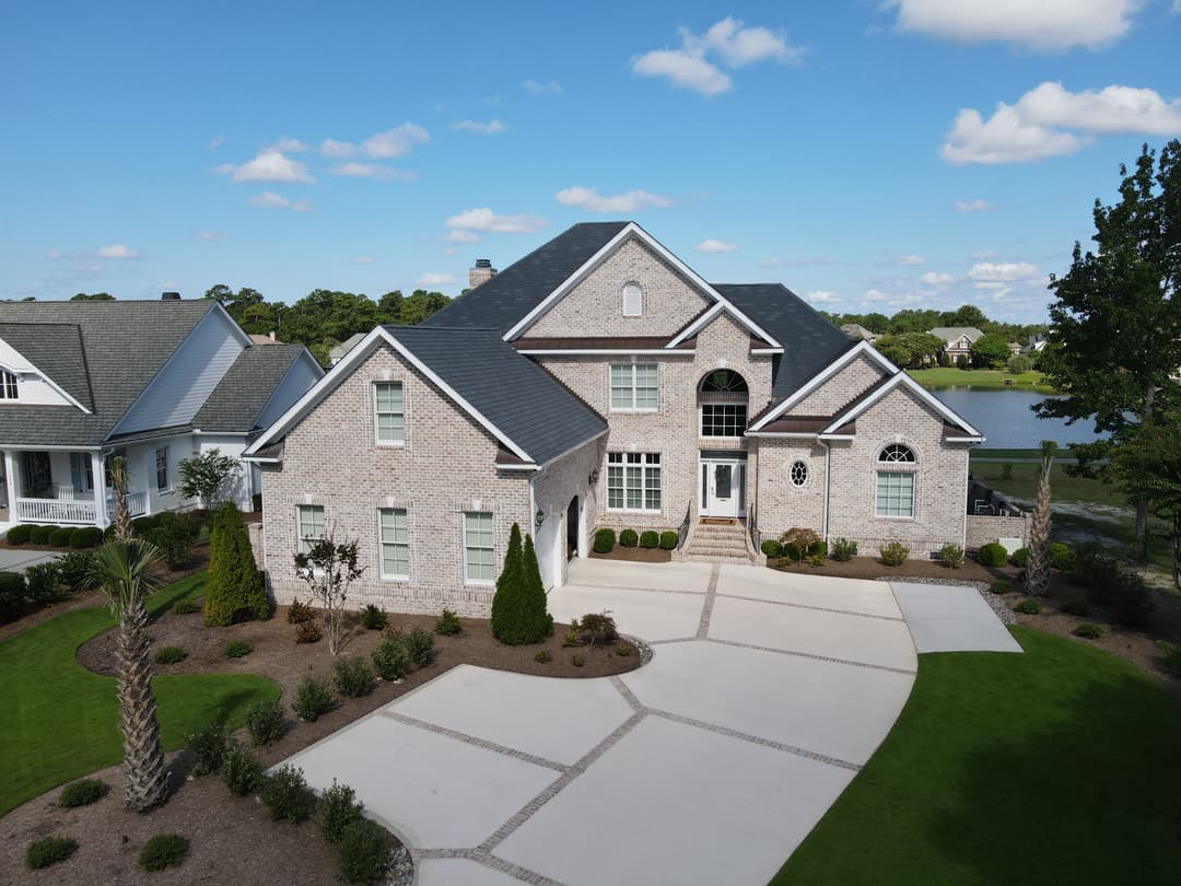 Elegant brick home with a landscaped yard and driveway, overlooking a serene lake.
