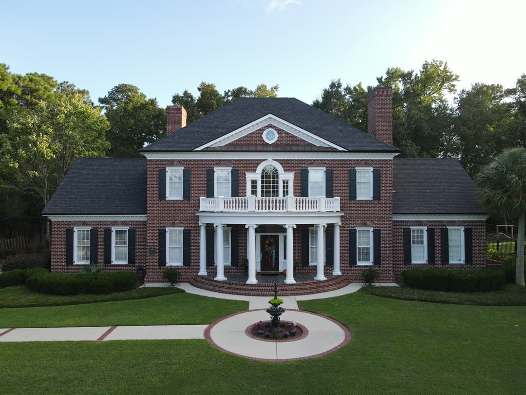 Elegant red brick Southern-style home with white columns, lush landscaping, and circular driveway.