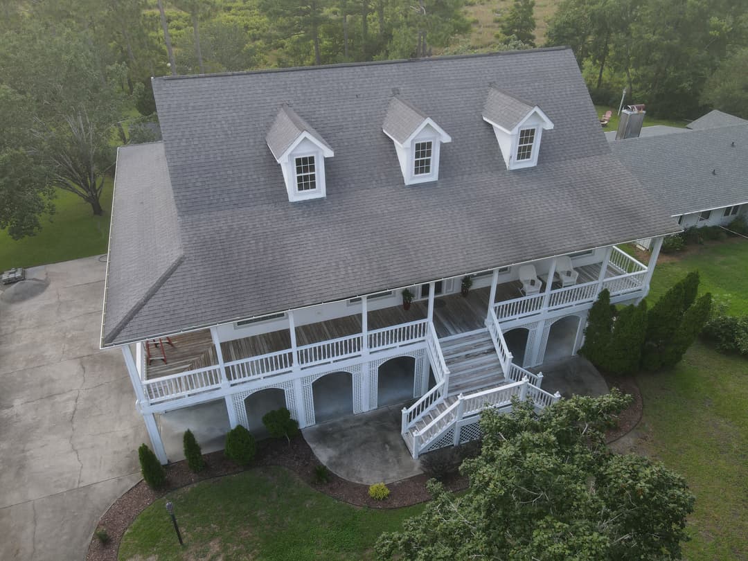 Aerial view of a two-story white house with a large porch and green surroundings.