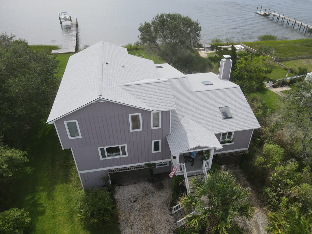 Aerial view of a purple two-story house with a porch, surrounded by greenery and waterfront.