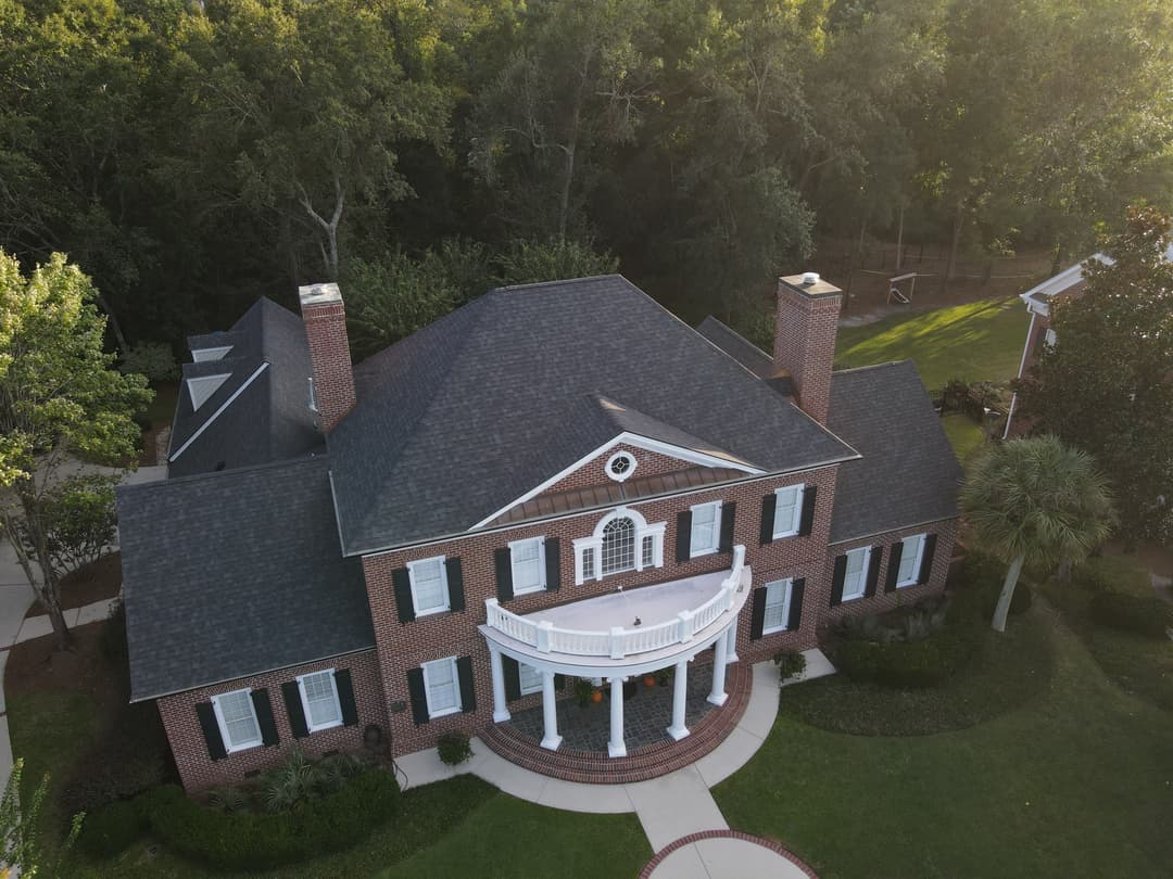 Aerial view of a classic brick mansion with white columns and landscaped surroundings.