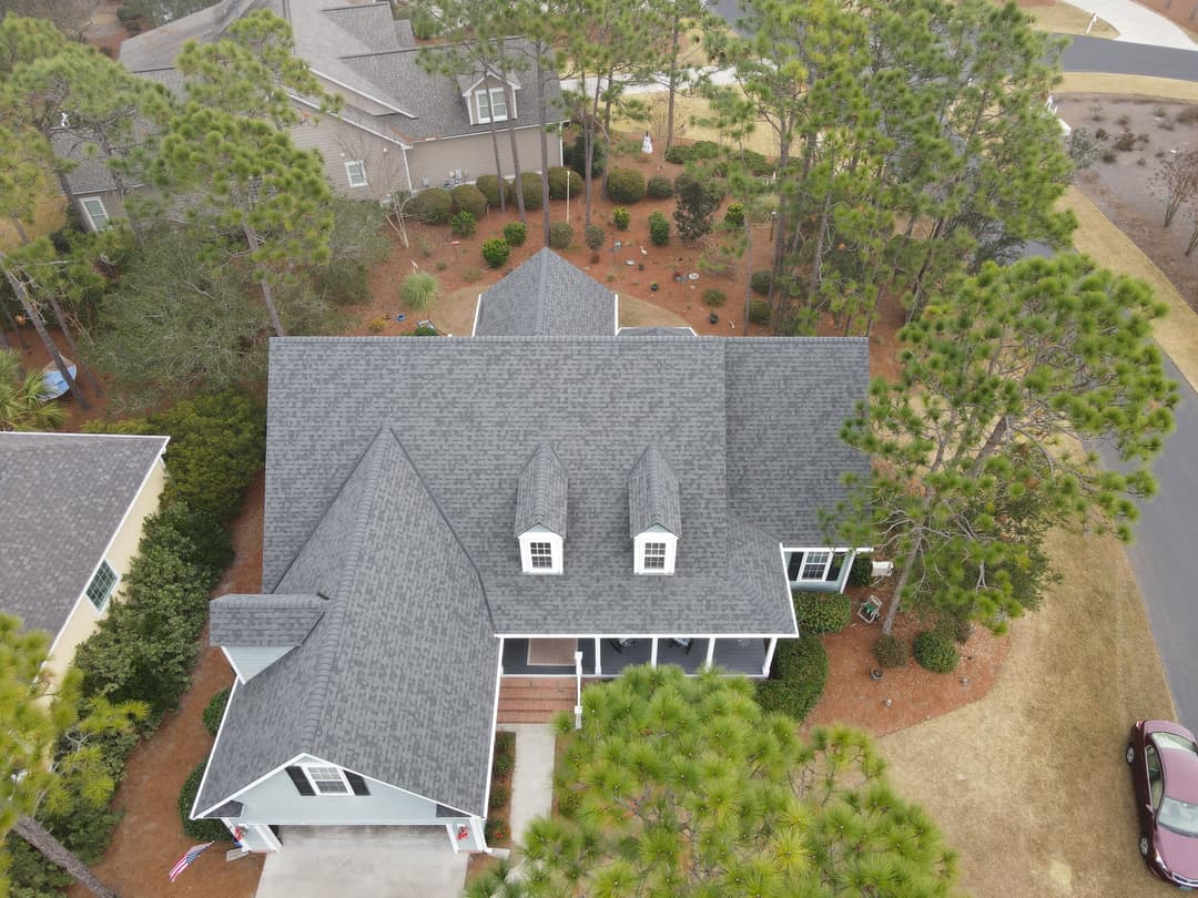 Aerial view of a suburban home with a gray roof surrounded by pine trees.