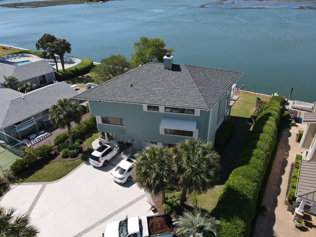 Aerial view of a waterfront home with palm trees, parking area, and nearby swimming pool.