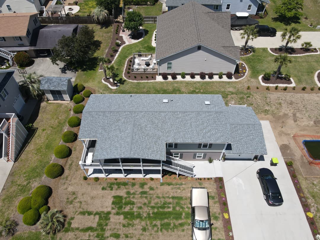 Aerial view of a modern home with gray roof, landscaped yard, and adjacent vehicles.