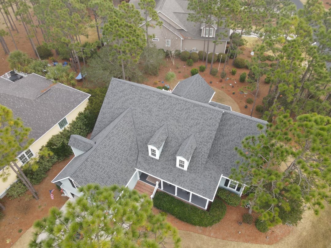 Aerial view of a spacious house with a gray roof surrounded by pine trees.