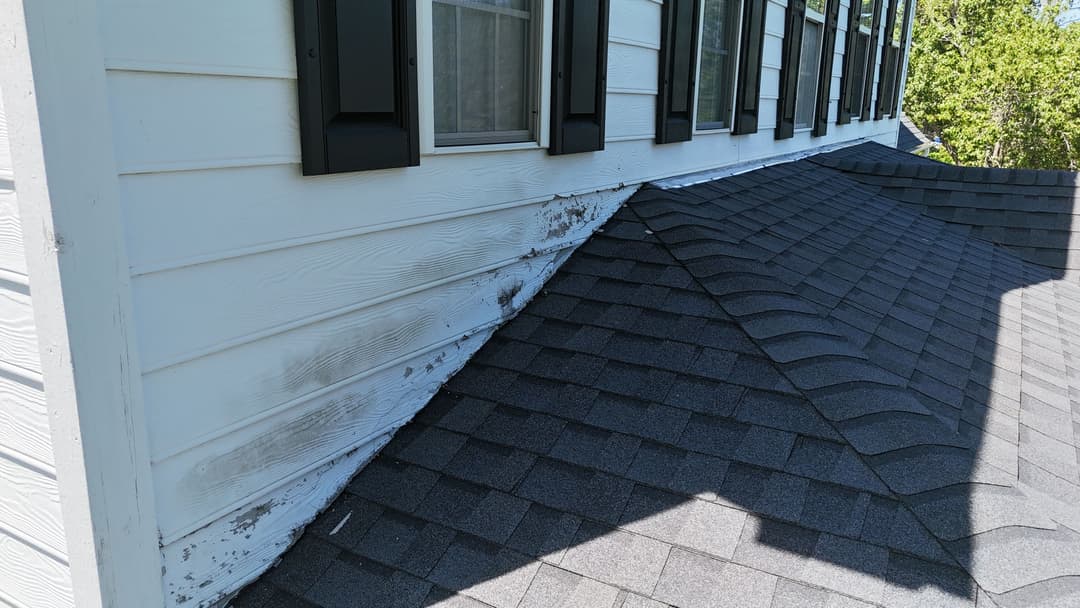 Weathered siding and a shingled roof showing signs of wear near a residential home.