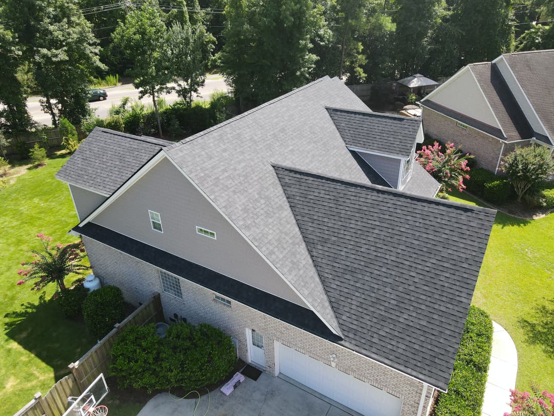 Aerial view of a modern home with a gray roof and lush green landscaping.