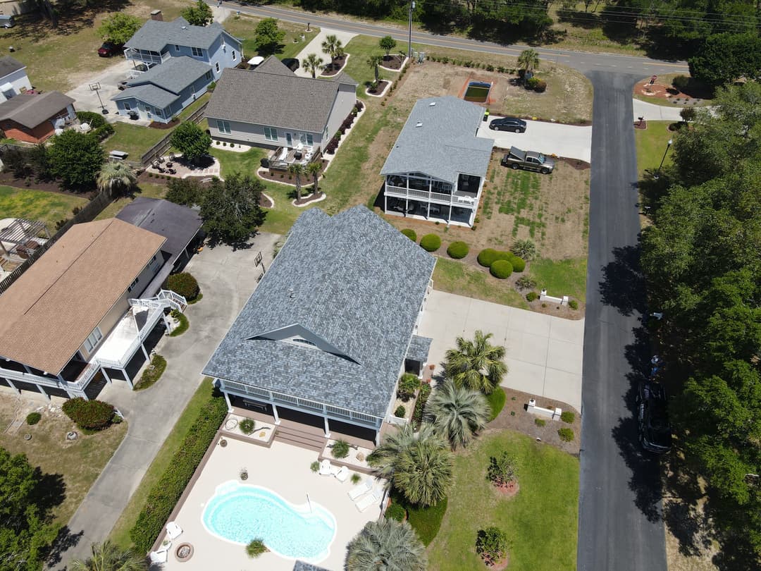 Aerial view of residential neighborhood featuring houses, a pool, and landscaped gardens.