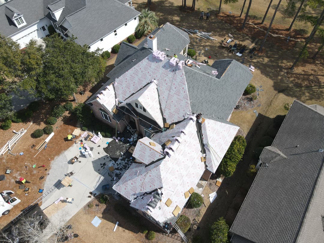 Aerial view of a residential roof being replaced, surrounded by construction debris and materials.