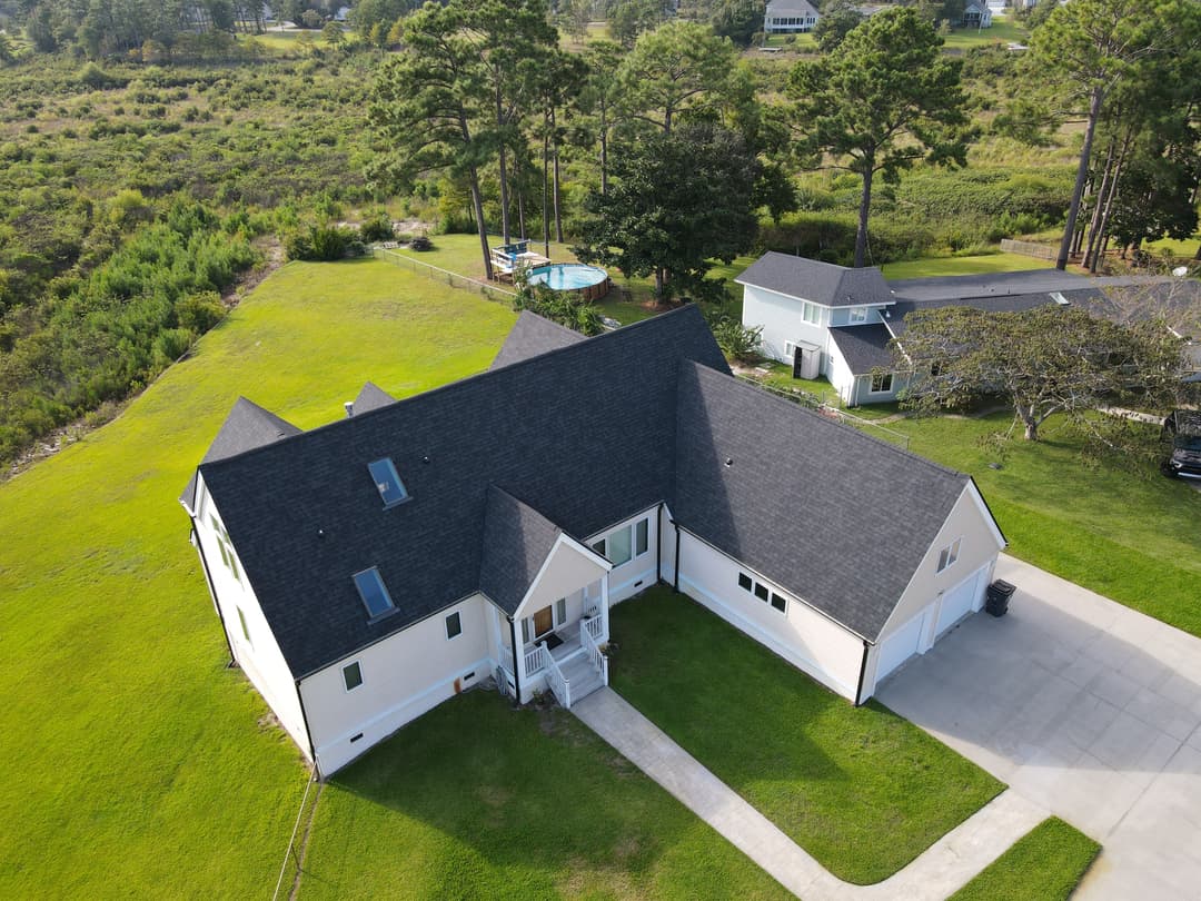 Aerial view of a modern house with a black roof, surrounded by green lawns and trees.