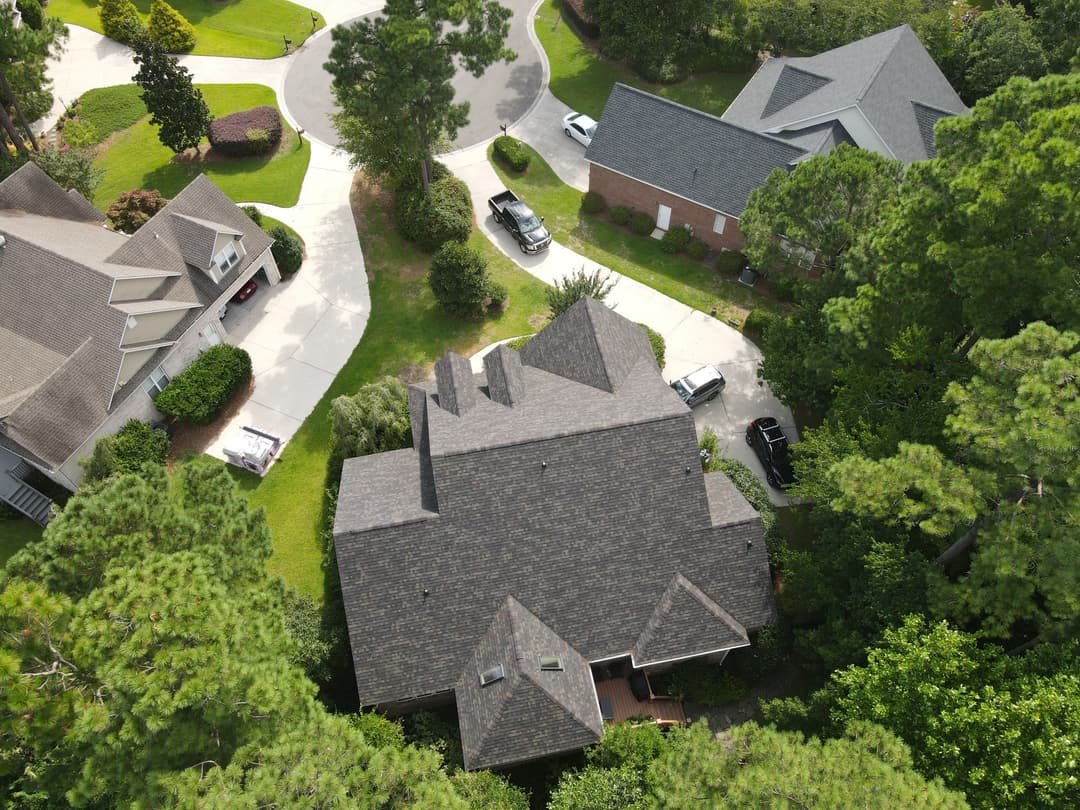 Aerial view of suburban neighborhood with houses surrounded by trees and parked cars.