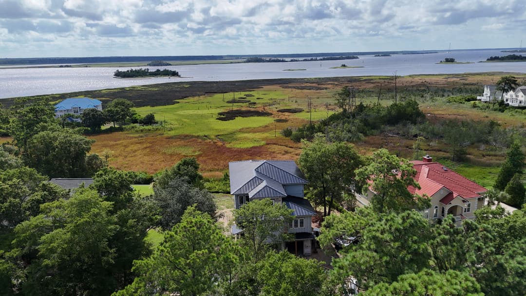 Aerial view of waterfront homes near lush green fields and a serene bay landscape.