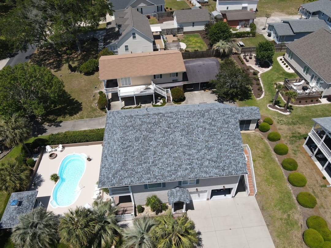 Aerial view of suburban homes with a pool and landscaped yard in a sunny neighborhood.