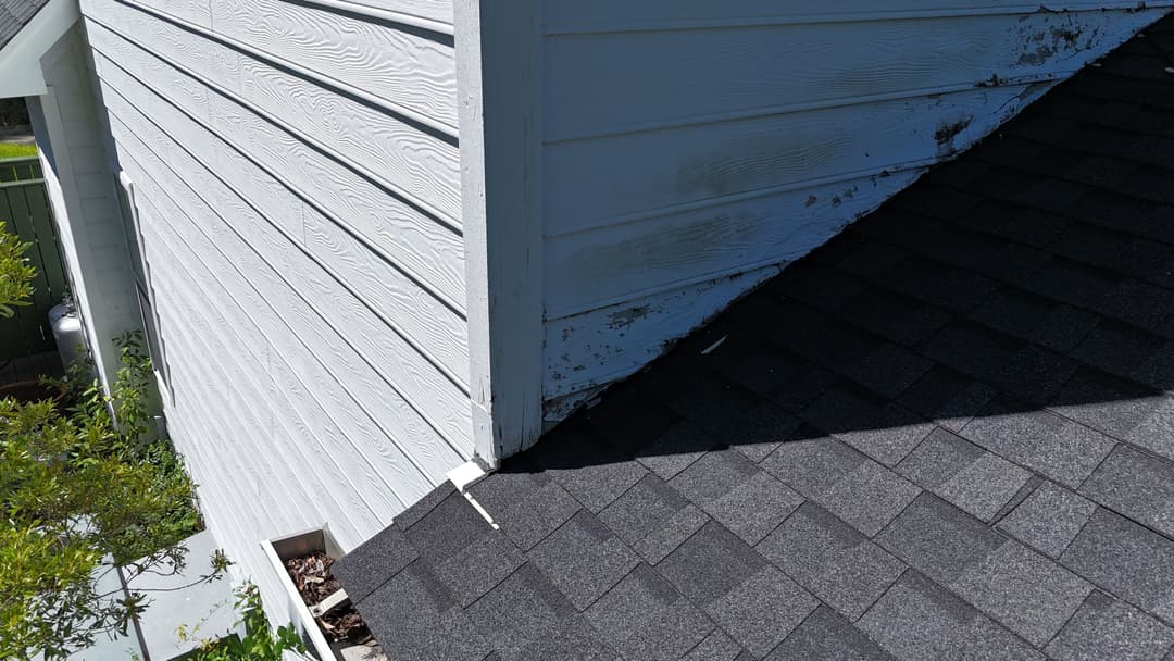 Roof corner showing damaged siding and shingles in need of repair.