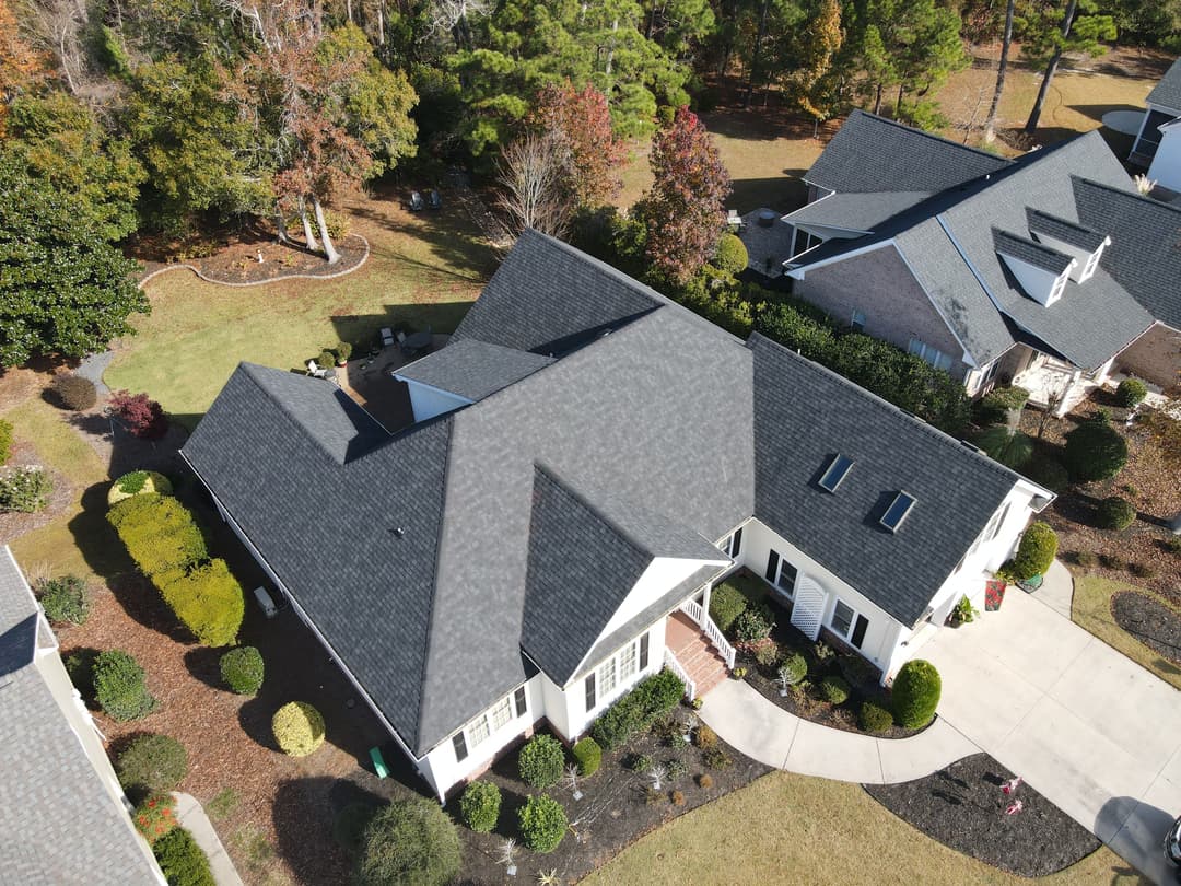 Aerial view of a modern home with a gray roof surrounded by landscaped yard and trees.