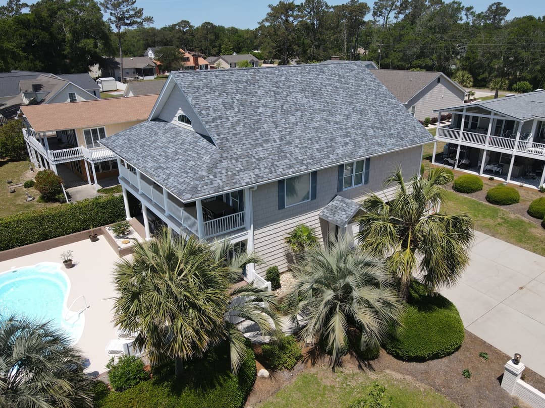 Aerial view of a modern house with palm trees and a pool in a residential neighborhood.