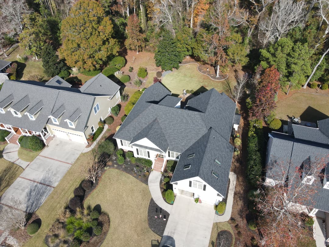 Aerial view of a well-manicured suburban home with a gray roof and landscaped yard.