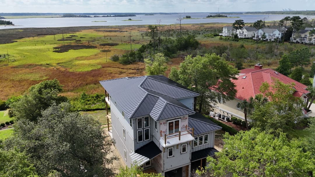 Aerial view of a modern house with a metal roof near a scenic lake and lush green landscape.