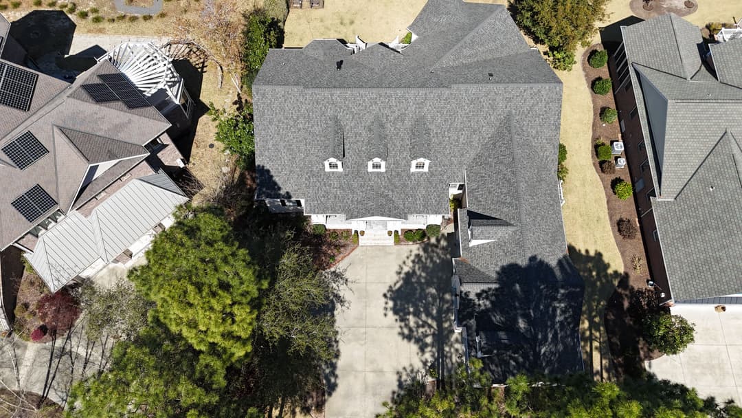 Aerial view of a large residential home with a paved driveway and landscaped yard.