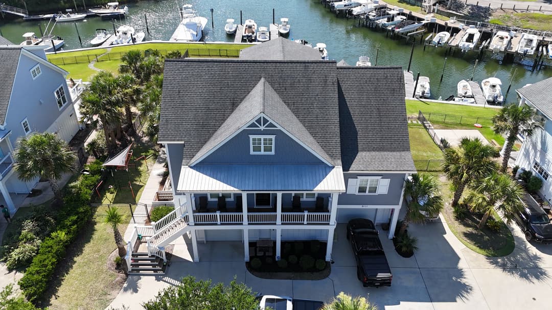 Aerial view of a coastal home near a marina with parked boats and palm trees.