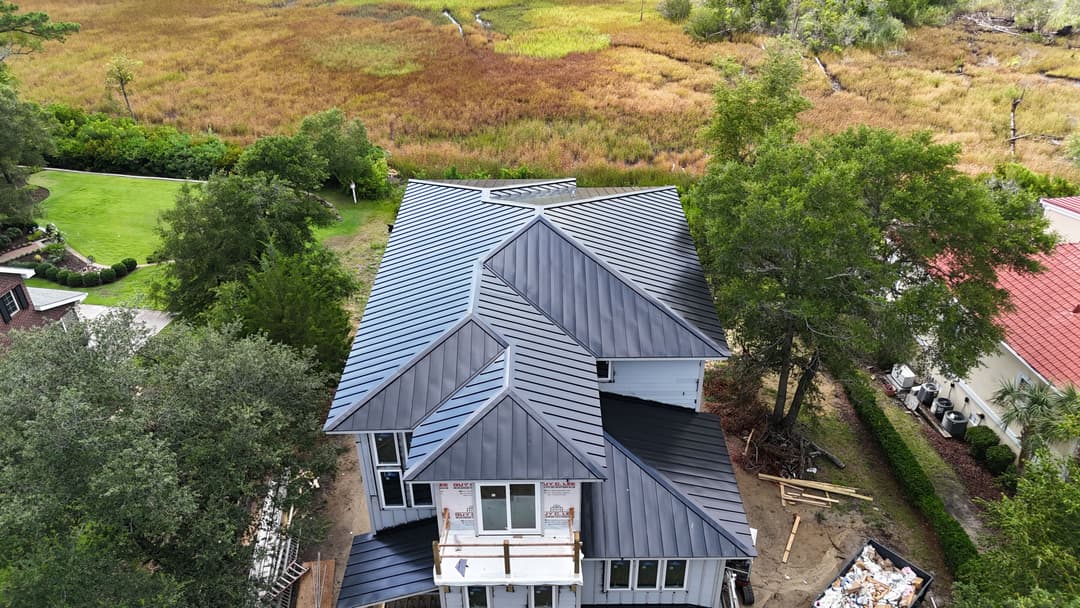 Aerial view of a modern house with a metal roof, surrounded by vibrant green and brown fields.