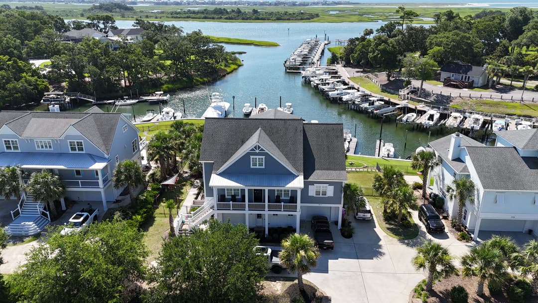 Aerial view of a waterfront home near a marina with boats and lush greenery.