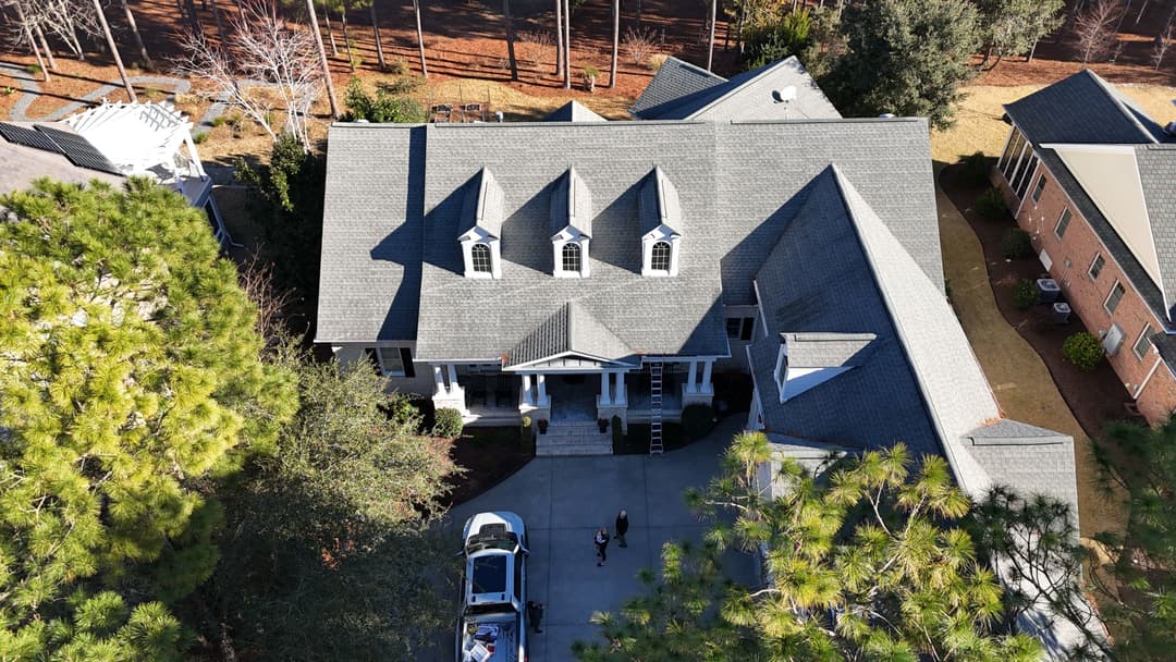 Aerial view of a large, elegant home with a gray roof and front entrance surrounded by trees.