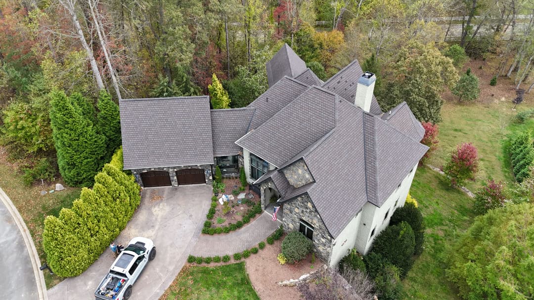 Aerial view of a large stone house with a landscaped yard and parked car.