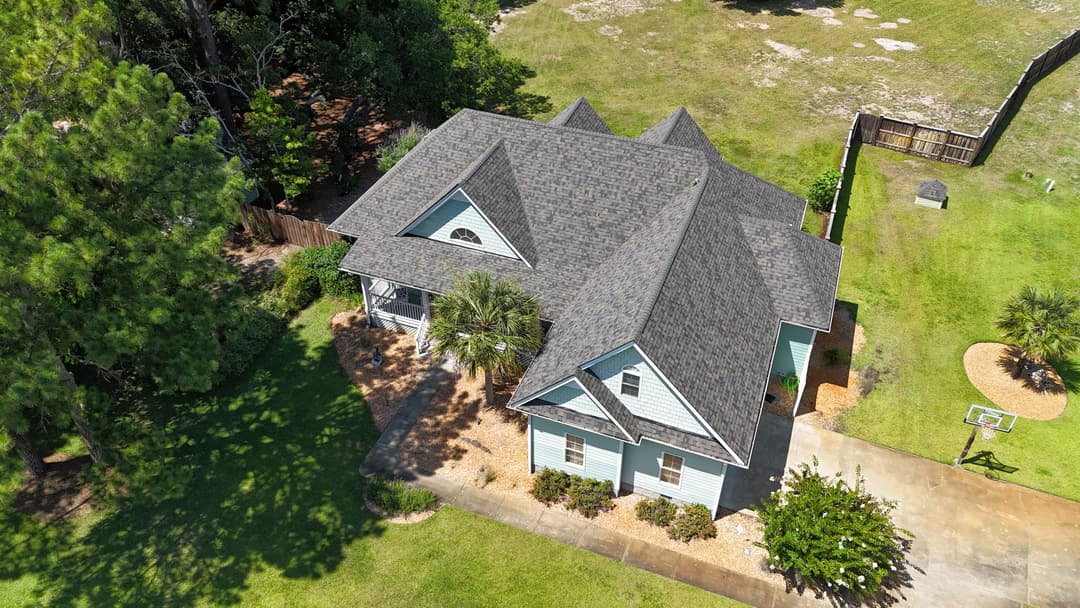 Aerial view of a large blue house with a gray roof surrounded by green grass and trees.