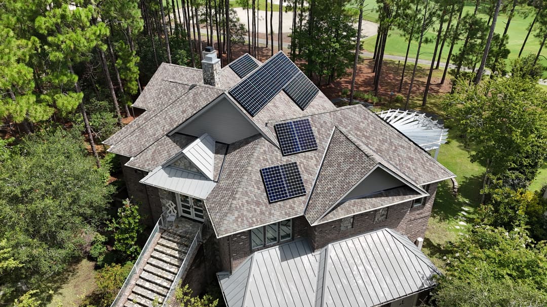 Aerial view of a home with solar panels on the roof surrounded by trees and a golf course.