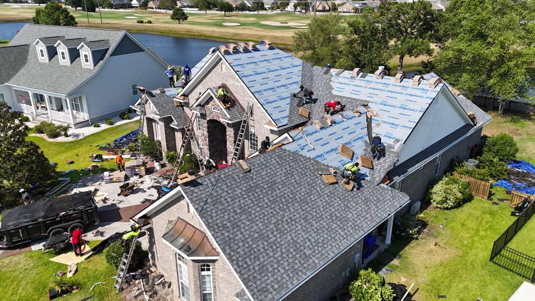 Roofing crew installing shingles on a residential house, surrounded by a golf course.