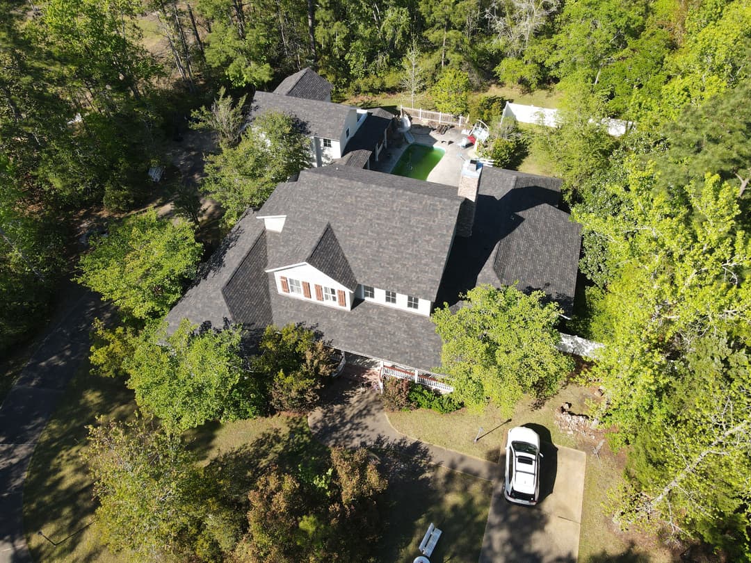 Aerial view of a two-story house surrounded by lush greenery and trees.