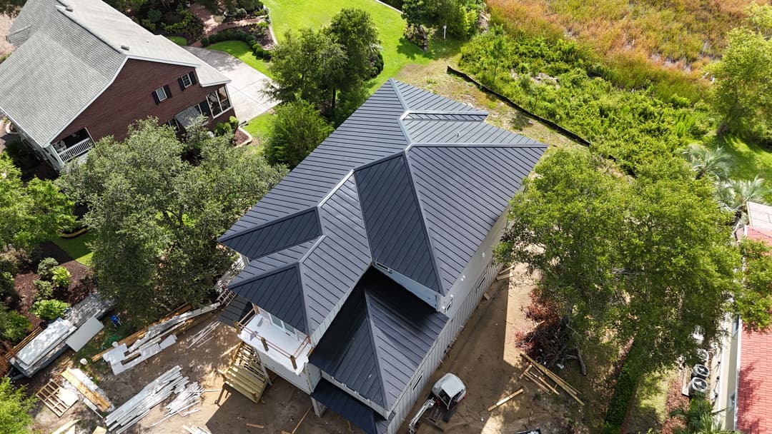 Aerial view of a modern house with a black metal roof surrounded by lush greenery.