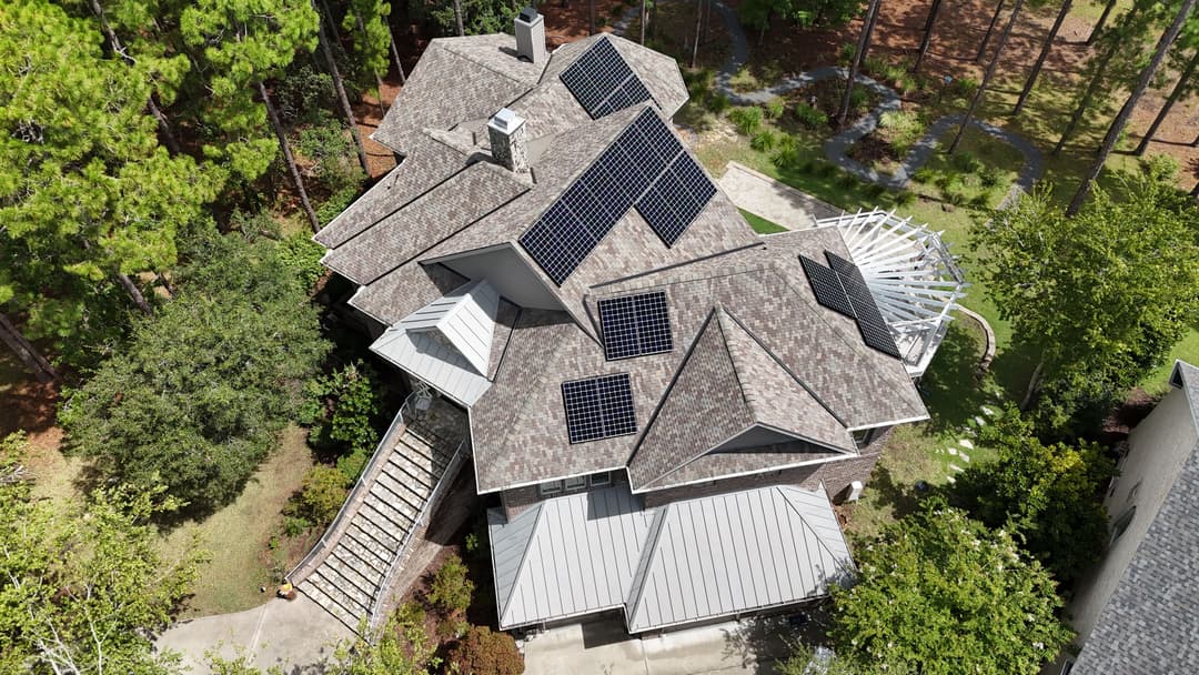 Aerial view of a house with solar panels and landscaped yard surrounded by trees.