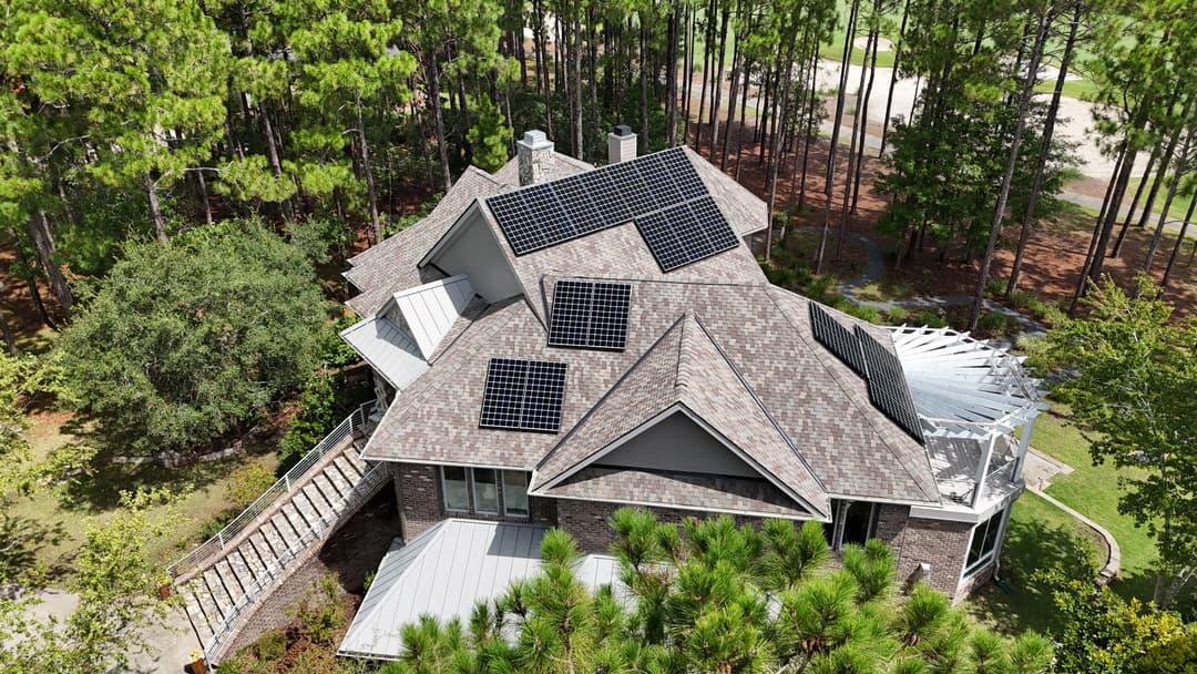 Aerial view of a modern home with solar panels on the roof surrounded by trees.